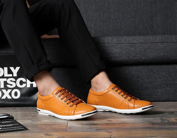Men's Valen tan leather low-top lace-up sneakers with white sole, styled with black trousers on wood floor