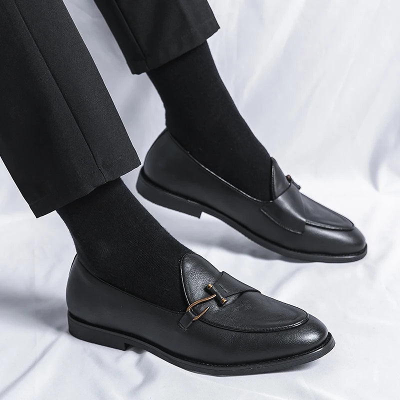 Black leather men's slip-on loafers with gold metal buckle detail, worn with black trousers and socks