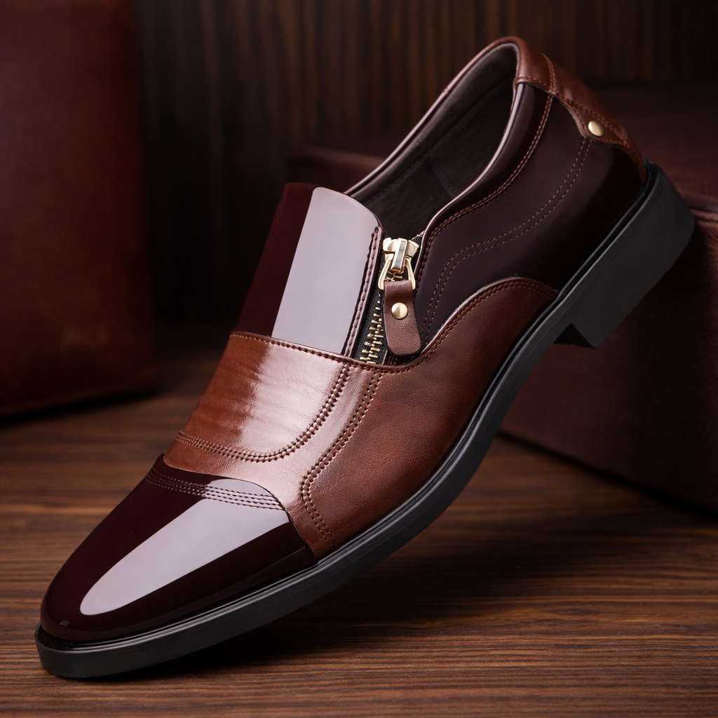 Brown two-tone patent leather slip-on loafers with gold side zipper closure and pointed toe on wooden surface
