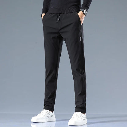 Men's black cotton drawstring joggers with elastic waistband, side pockets, and ribbed cuffs, paired with white sneakers.