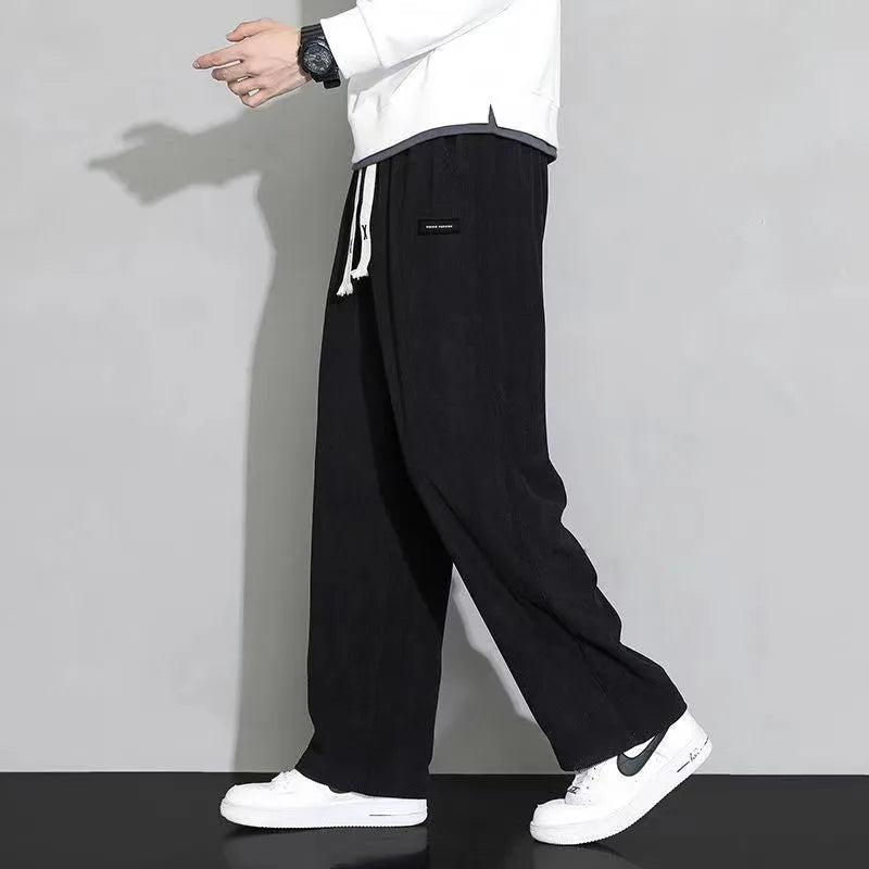 Men's black corduroy wide-leg sweatpants with drawstring waist, paired with white hoodie and Nike sneakers.