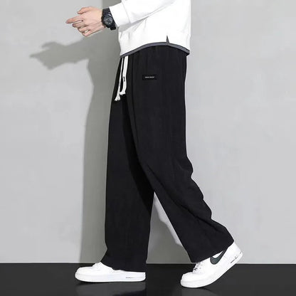 Men's black corduroy wide-leg sweatpants with drawstring waist, paired with white hoodie and Nike sneakers.