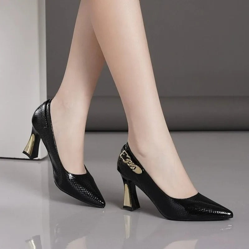 Black snakeskin-embossed leather block heel pumps with gold chain detail and metallic heel accent on women's feet