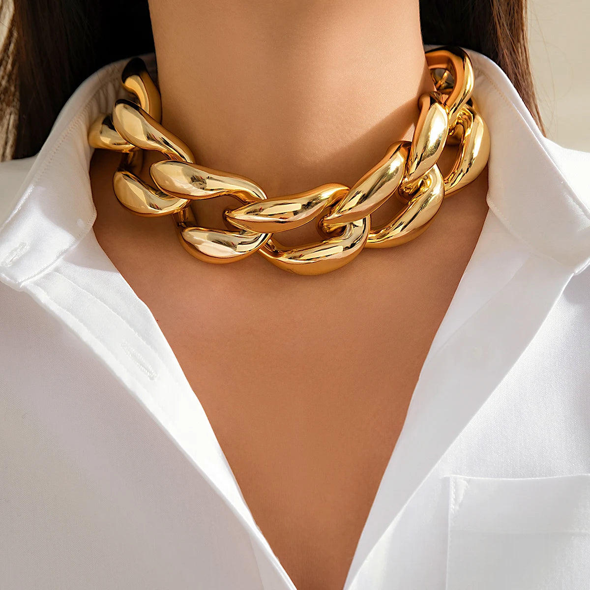 Chunky gold chain link choker necklace statement jewelry worn on woman's neck with white blazer