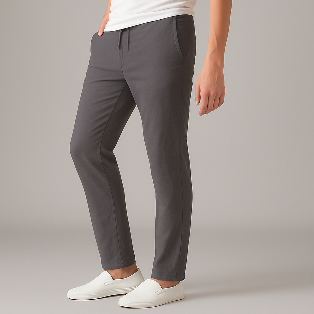 Man wearing slim-fit dark gray drawstring linen pants with white t-shirt and white slip-on sneakers, side view.