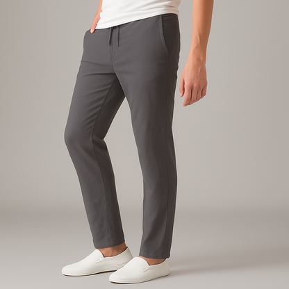 Man wearing slim-fit dark gray drawstring linen pants with white t-shirt and white slip-on sneakers, side view.