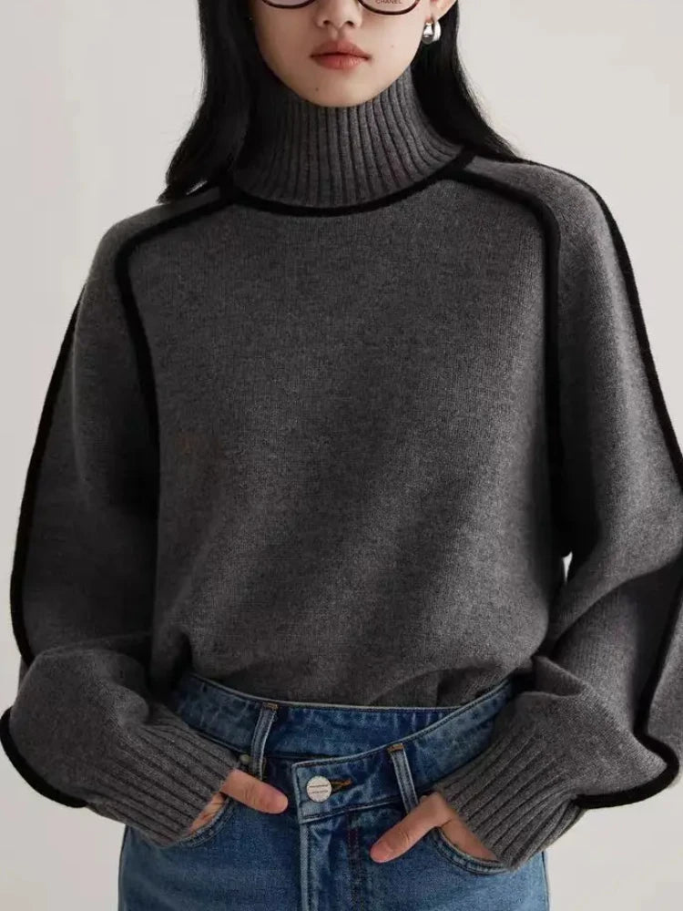 Gray turtleneck knit sweater with black contrast piping trim, long sleeves, worn with blue jeans