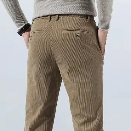 Man wearing khaki corduroy slim fit chino pants from behind, showing back pocket detail and straight leg silhouette.