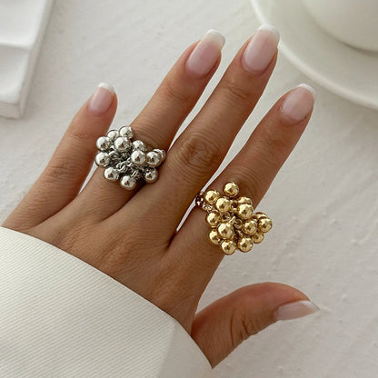 Woman's hand wearing two adjustable beaded cluster rings in silver and gold with dangling ball charms