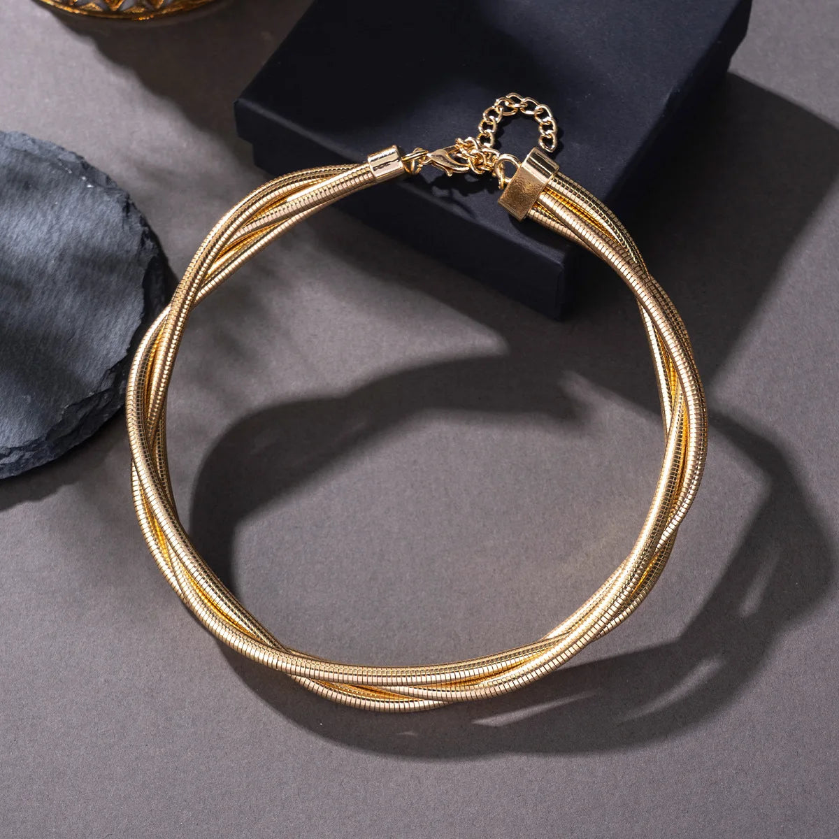 Gold multi-strand twisted snake chain choker necklace with lobster clasp and extender chain on gray surface