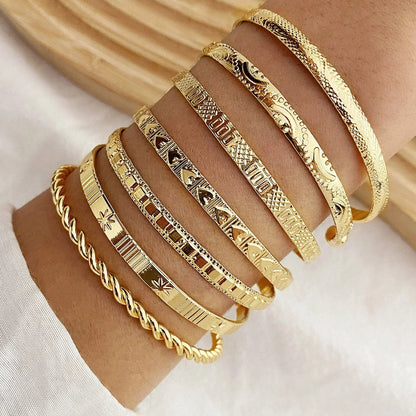 Set of 6 etched gold bangle bracelets with geometric patterns stacked on woman's wrist