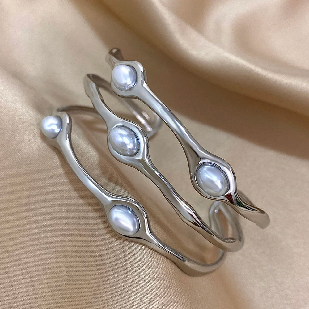 Silver tone open cuff bangles with embedded freshwater pearls in wavy design, stacked on satin fabric