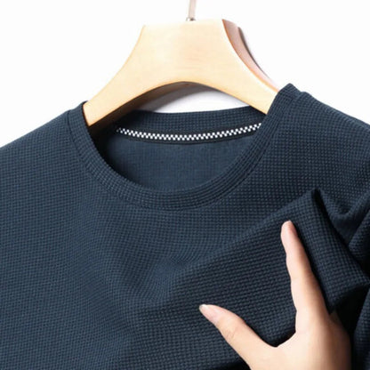 Dark navy waffle knit crewneck t-shirt on wooden hanger, hand showing textured fabric detail, checkered inner collar tag