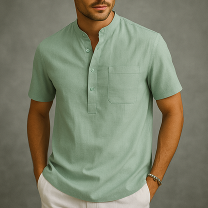 Man wearing a sage green linen short-sleeve henley shirt with band collar, chest pocket, and partial button placket.