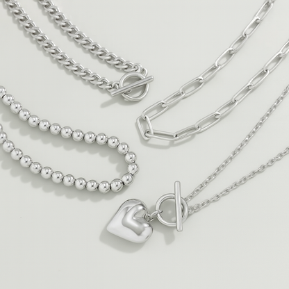 Silver layered necklace set featuring curb chain, bead chain, paperclip chain, and heart pendant with toggle clasps