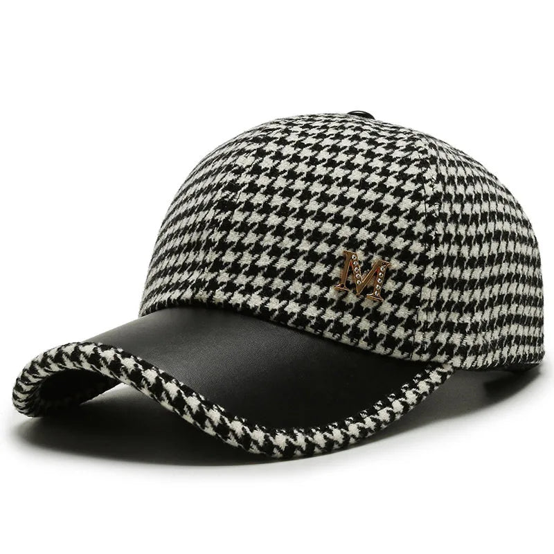 Black and white houndstooth baseball cap with leather brim and gold metal M emblem on white background