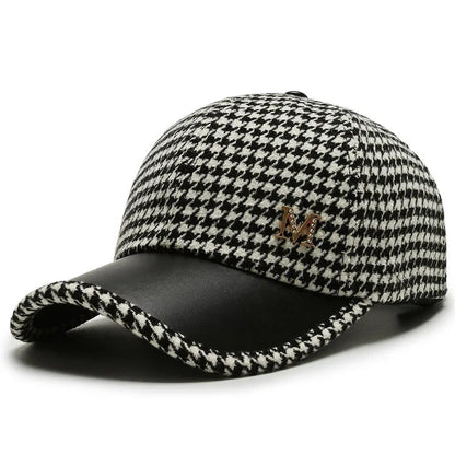 Black and white houndstooth baseball cap with leather brim and gold metal M emblem on white background