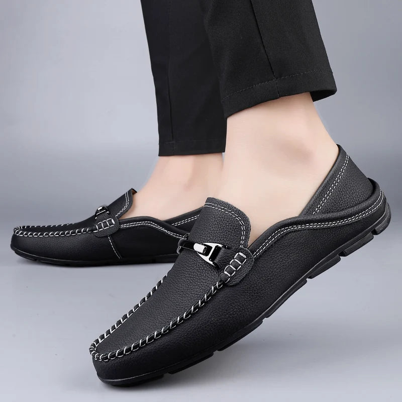 Black men's leather slip-on loafers with contrast stitching and silver metal buckle detail, paired with black trousers