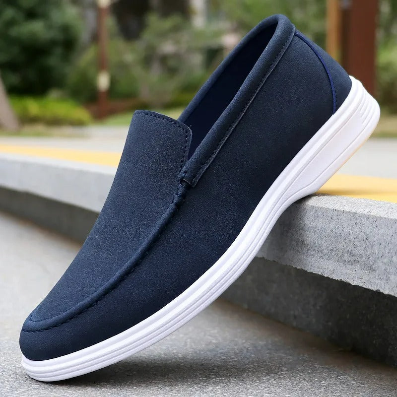 Navy blue suede slip-on loafers for men with white rubber sole, displayed on concrete steps outdoors