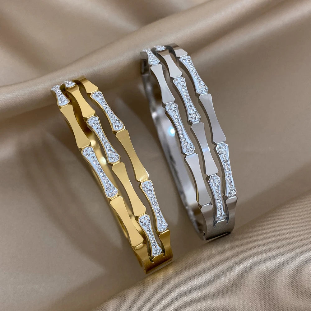 Gold and silver geometric bangle bracelets with crystal stone accents displayed on beige satin fabric