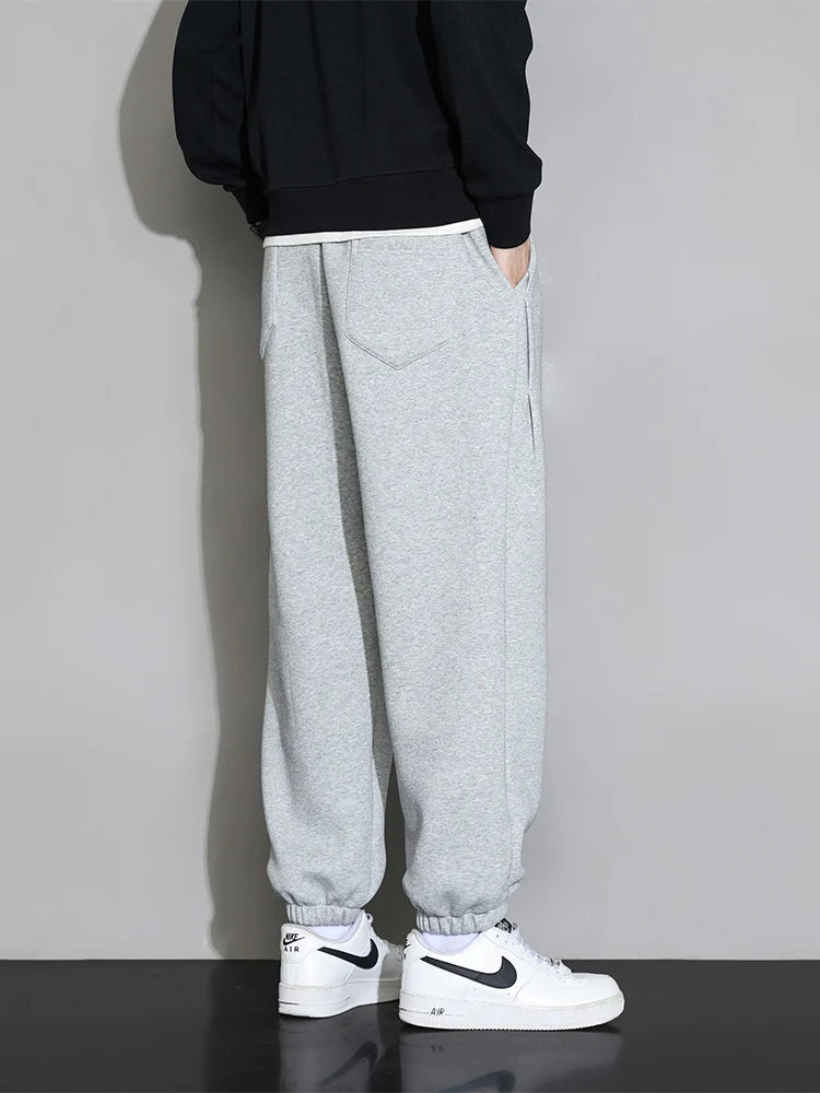 Men's gray relaxed fit cotton joggers with elastic cuffs and black hoodie, worn with white Nike Air Force 1 sneakers