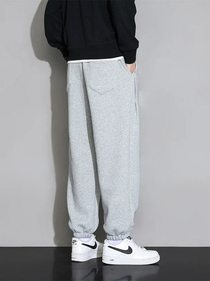 Men's gray relaxed fit cotton joggers with elastic cuffs and black hoodie, worn with white Nike Air Force 1 sneakers