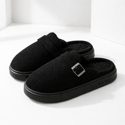 Black suede slip-on mule slippers with silver buckle detail, plush sherpa lining, and chunky rubber sole.