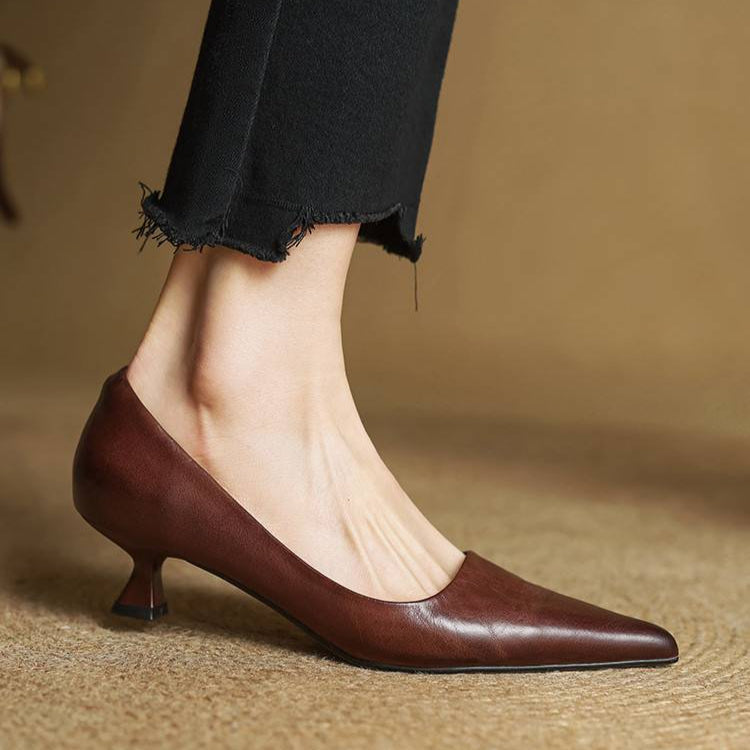Women's brown leather pointed-toe pumps with kitten heel, styled with black frayed-hem cropped jeans on neutral background.