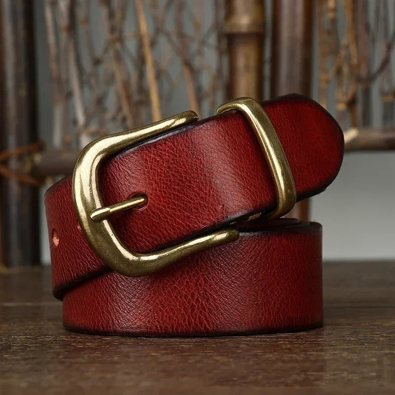 Red genuine leather men's belt with antique brass pin buckle, coiled on wooden surface, vintage style
