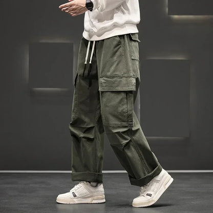 Men's olive green wide-leg cargo pants with multiple pockets and rolled cuffs paired with white sneakers