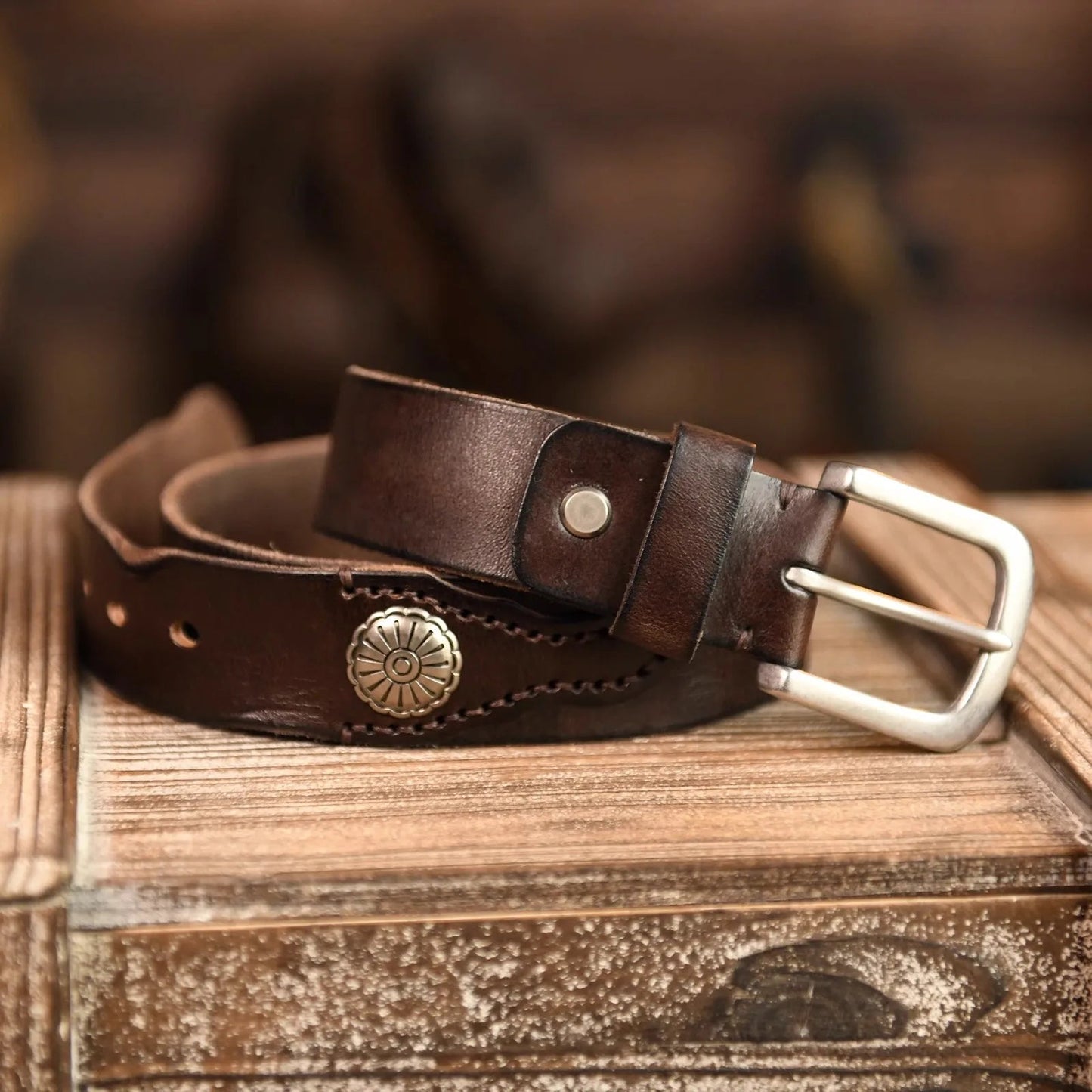 Dark brown leather belt with silver metal concho decorations and hand-stitched details on wooden surface