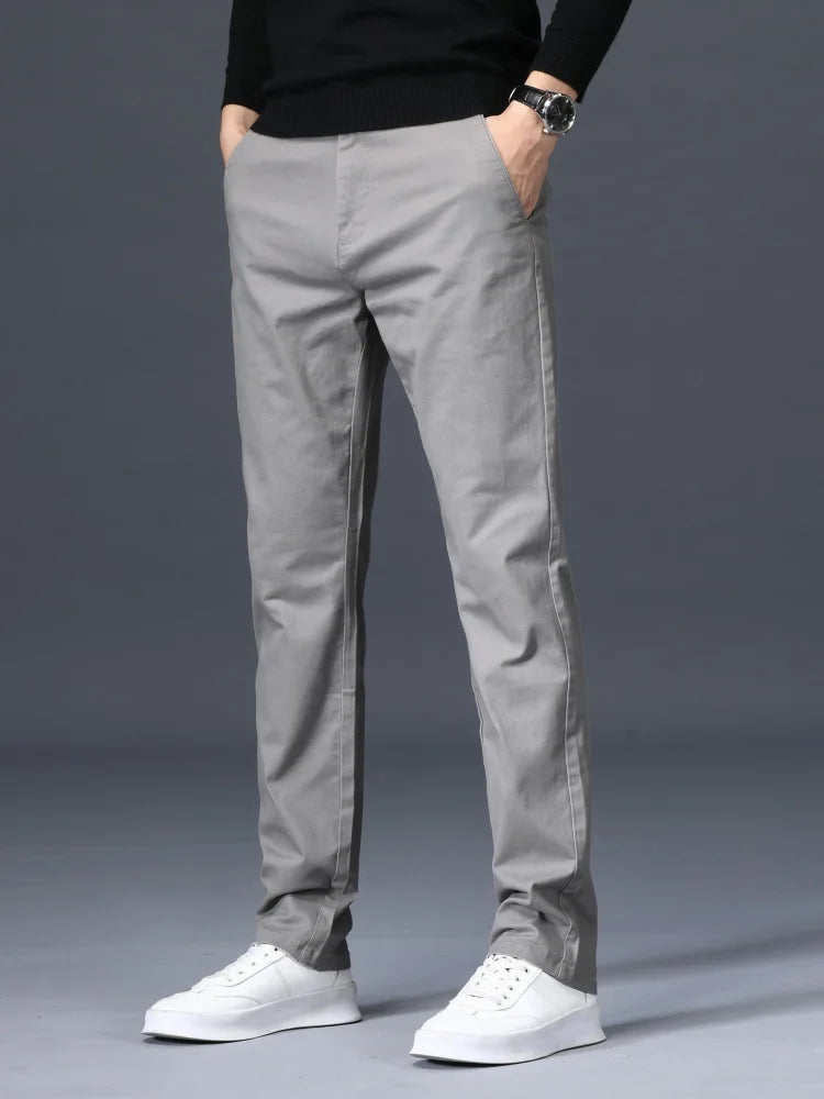 Man wearing slim-fit light gray cotton dress pants with black sweater and white sneakers, front view on gray background
