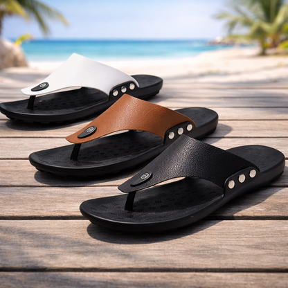 Men's leather thong flip-flop sandals in black, tan, and white with silver studs, displayed on wooden deck near beach.