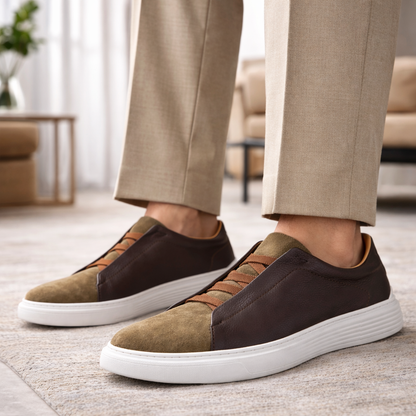 Men's orthopedic sneakers in dark brown leather and olive suede with tan elastic laces and white sole, styled with beige trousers.