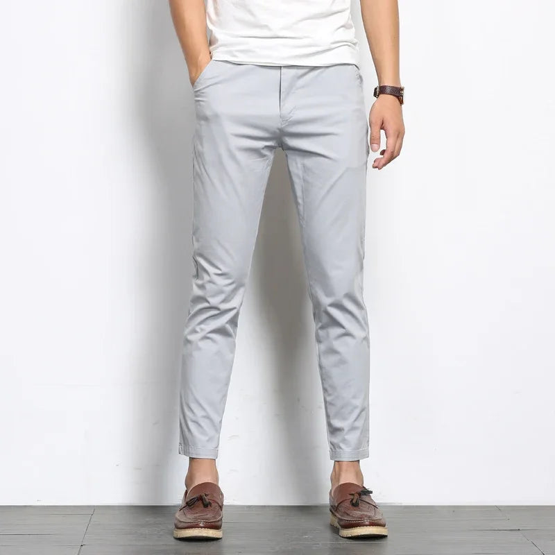 Man wearing slim fit light gray cotton chino pants with white tee and brown loafers, cropped ankle length style.