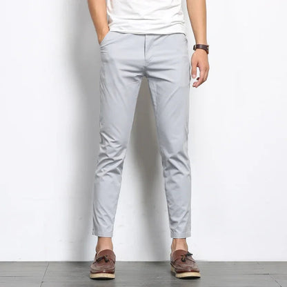 Man wearing slim fit light gray cotton chino pants with white tee and brown loafers, cropped ankle length style.