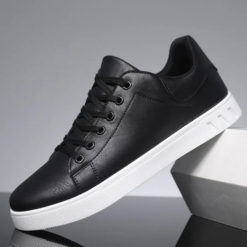 Black leather lace-up low-top men's sneakers with white sole, displayed on geometric white blocks against gray background