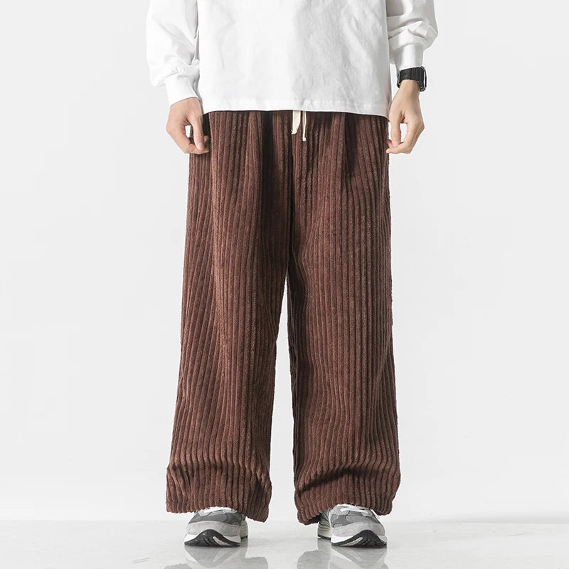 Brown wide-leg corduroy drawstring pants worn with white top and gray sneakers, featuring vertical ribbed texture