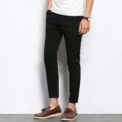 Man wearing black slim fit cotton chino pants with white tee and brown tassel loafers against white wall
