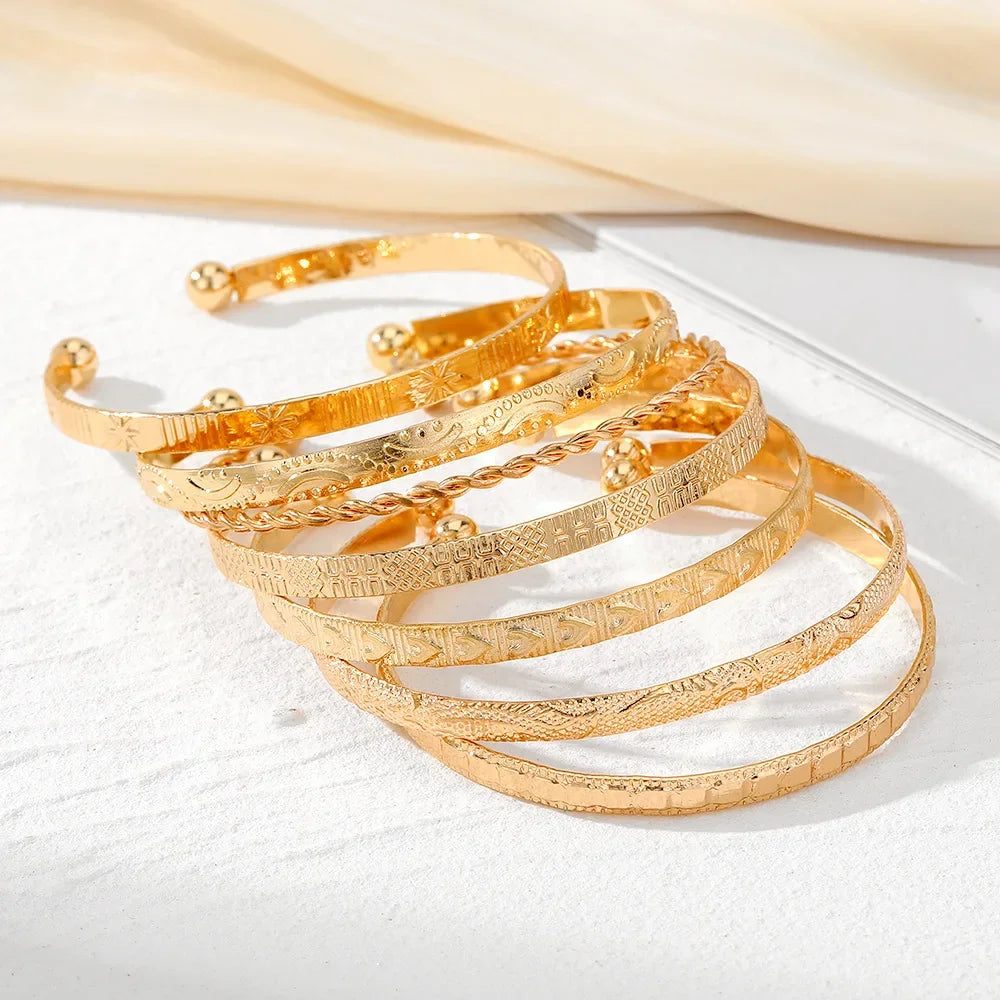 Set of six gold-tone etched bangle bracelets with various engraved patterns, stacked on a white surface.