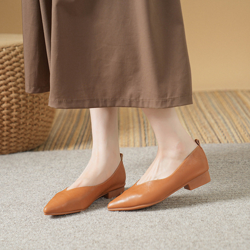Women's tan leather pointed-toe block heel pumps paired with a brown midi skirt on a gray carpet floor.