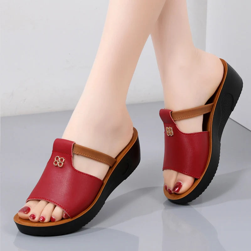 Red women's platform slide sandals with cutout detail, tan accent strap, gold embellishment, and black wedge sole.