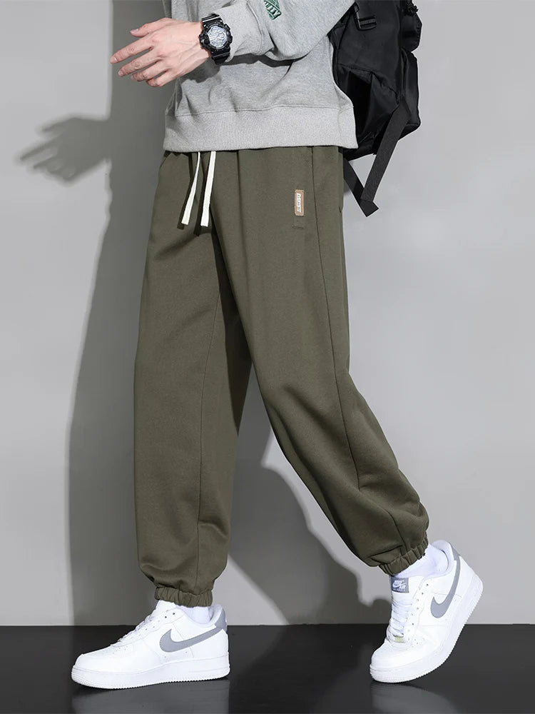 Men's olive green relaxed fit cotton jogger pants with drawstring waist and elastic cuffs, paired with white Nike sneakers