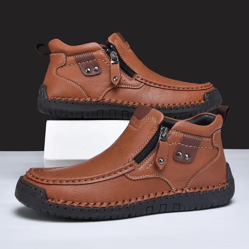 Brown leather men's ankle boots with side zipper, hand-stitched detailing, and rubber sole, displayed on white surface.