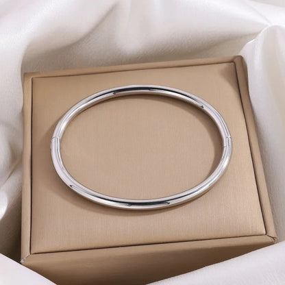 Polished silver bangle bracelet displayed on beige gift box with white satin fabric background