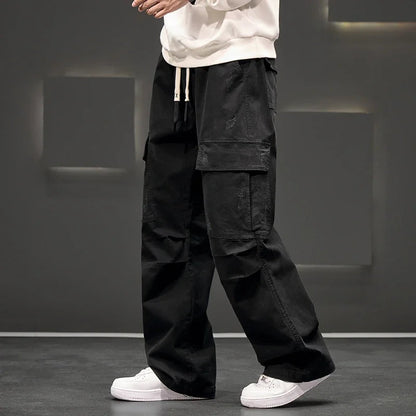 Black wide-leg men's cargo pants with side pockets and drawstring waist, paired with white sneakers and cream hoodie.