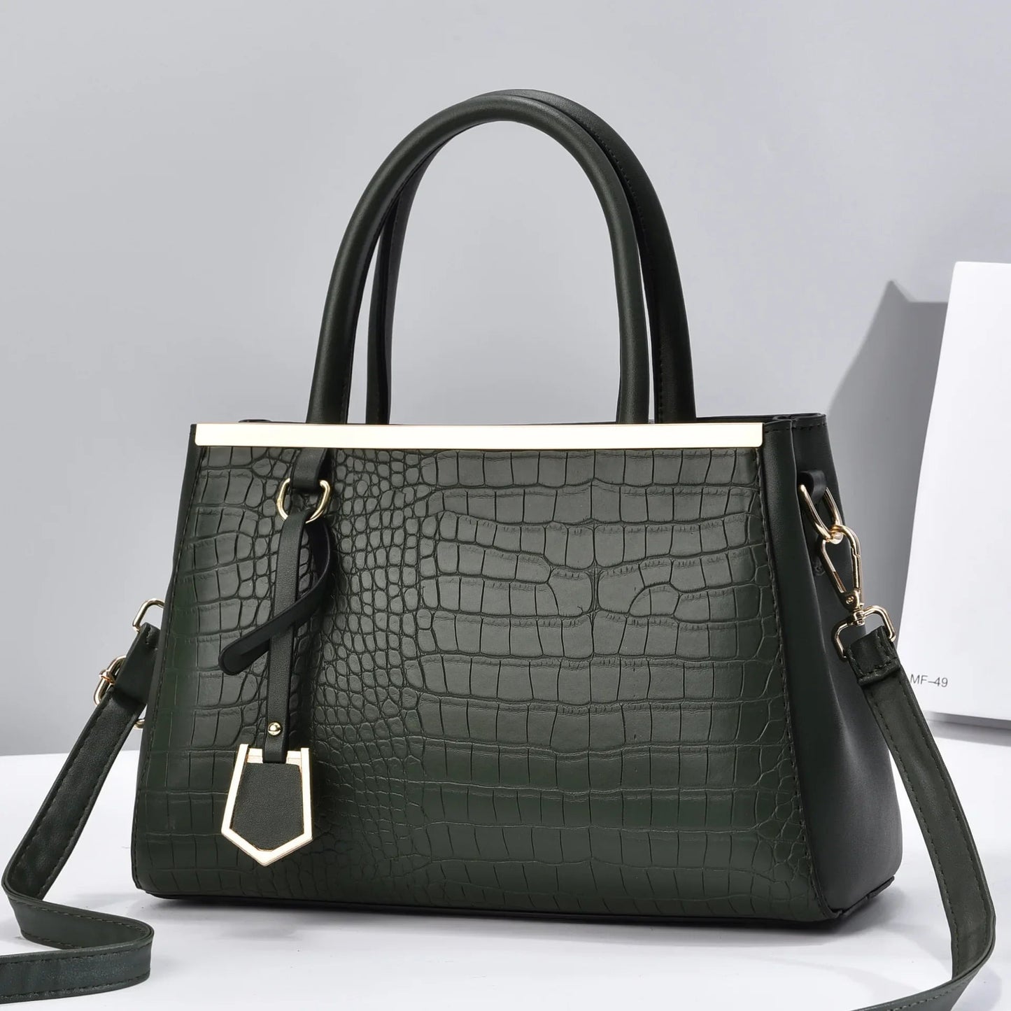 Dark green croc-embossed structured handbag with black top handles, gold-tone hardware bar detail, and removable crossbody strap.