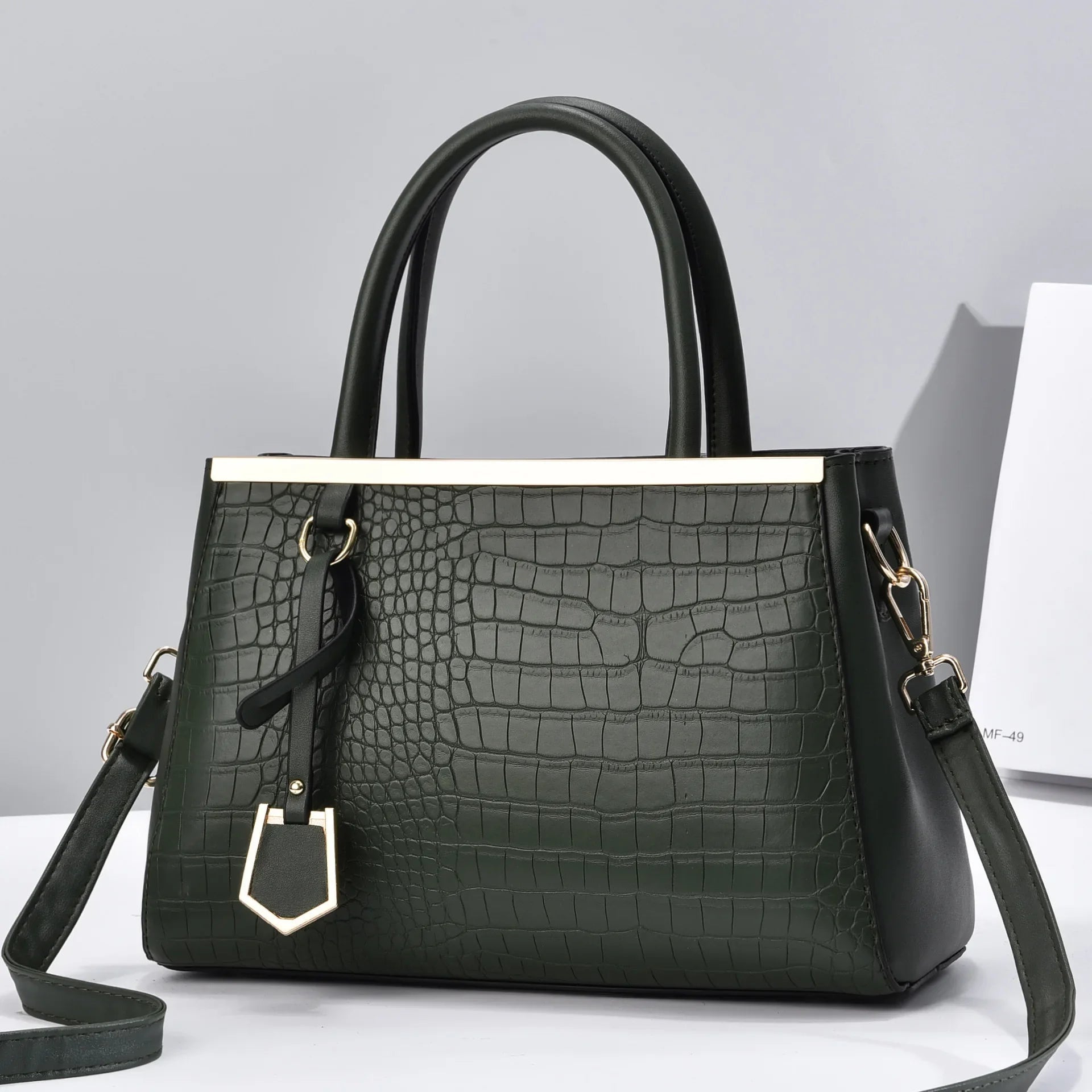 Dark green croc-embossed structured handbag with black top handles, gold-tone hardware bar detail, and removable crossbody strap.