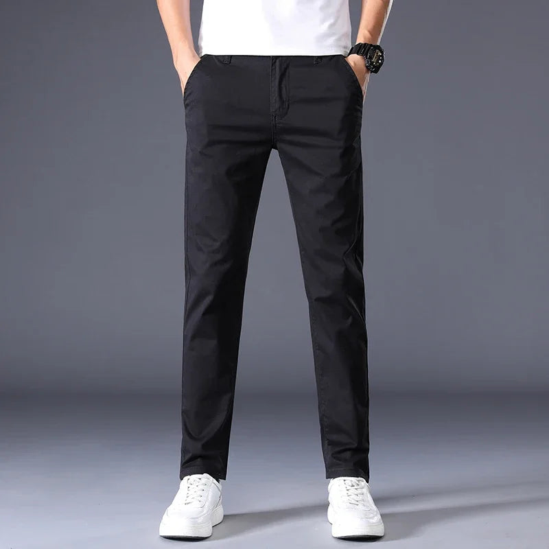 Men's slim fit black cotton dress pants worn with white sneakers and t-shirt, straight leg casual style