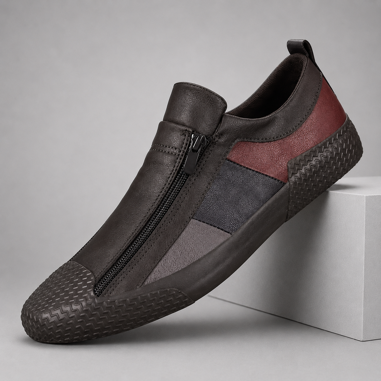 Dark brown leather slip-on sneakers with front zipper, red and gray color-block panels, and textured rubber sole.